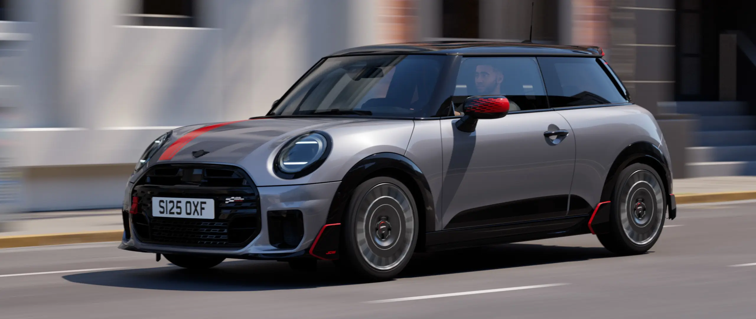 MINI Cooper 3도어 (멜팅 실버), 존 쿠퍼 웍스 미러 캡 및 보닛 데칼 (칠리 레드), 루프 스포일러 및 윙렛 (블랙), 도시 도로를 따라 달리는 모습 - 전면 전망.