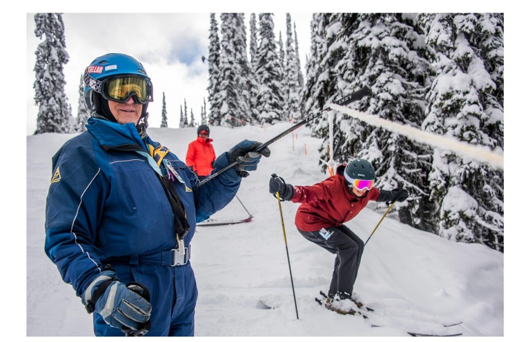 Image of three “Silver Sliders”, skiing down the mountain. One lifts a skiing pole with a rope, while another skis.