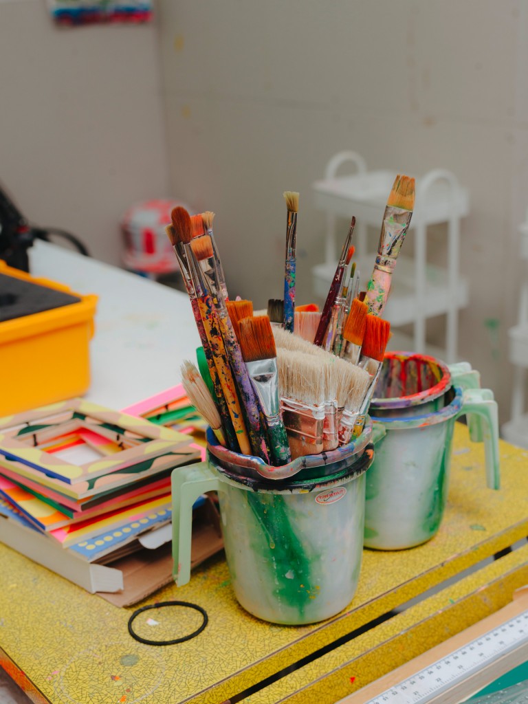 Alt-Tag: Two close-ups in Lakwena’s studio. One shows her creating a sketch, the other shows painting utensils. 